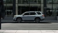 2023 Honda Pilot Sport shown in Sonic Gray Pearl with accessory crossbars standing by the building